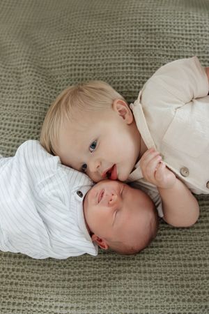 toddler boy and newborn baby boy laying on master bedroom brother giving kiss on cheek newborn photography kansas city