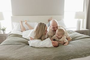 family laying on master bed looking at baby brother newborn photography kansas city