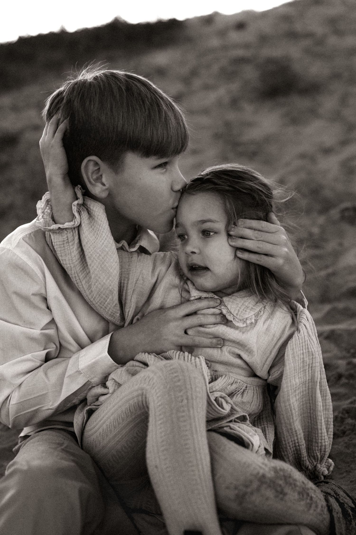 A tender black and white portrait in Denia of a young child comforting another child in a rustic outdoor setting. Denia family photographer