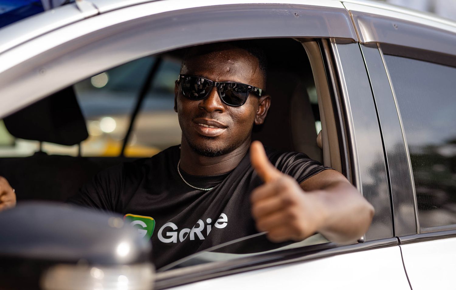 Driver wearing sunglasses and a Genie t-shirt gives thumbs up from car window.