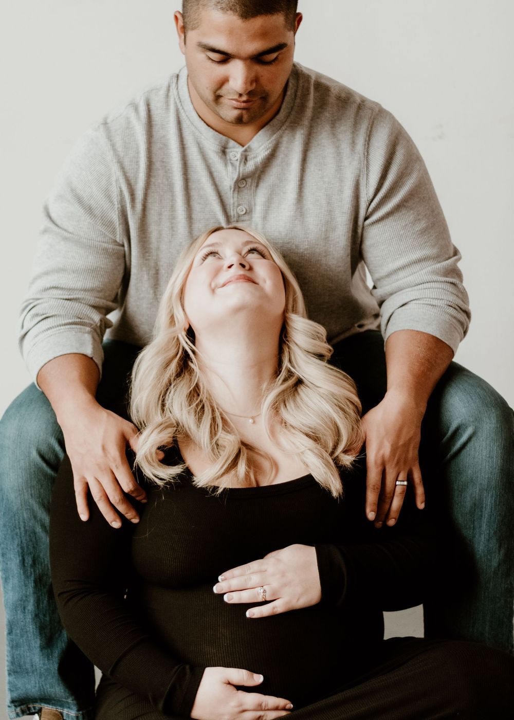 A couple shares an intimate moment together as she leans back with blonde hair cascading while he wears a gray sweater.