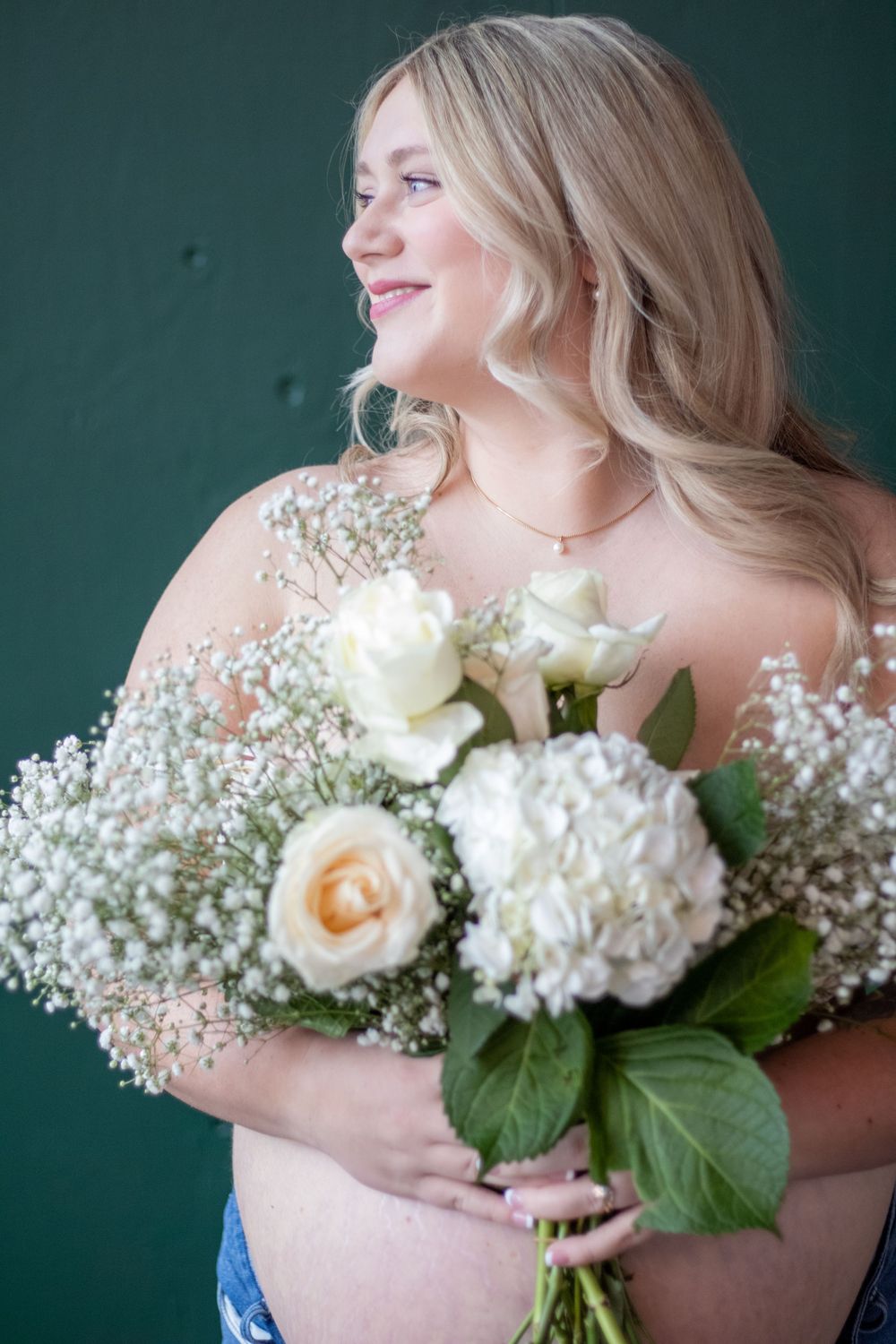A radiant bride holds a beautiful bouquet of white roses, hydrangeas and baby's breath against a deep green background.