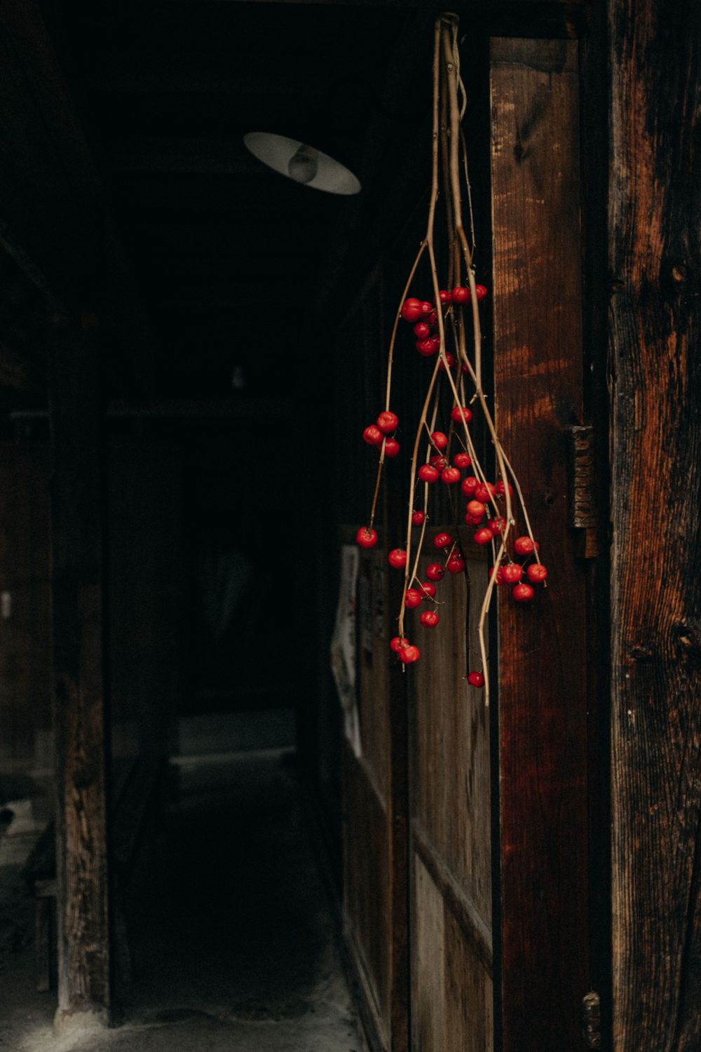 Red winter berries hanging against dark wooden beams in a traditional Japanese building.