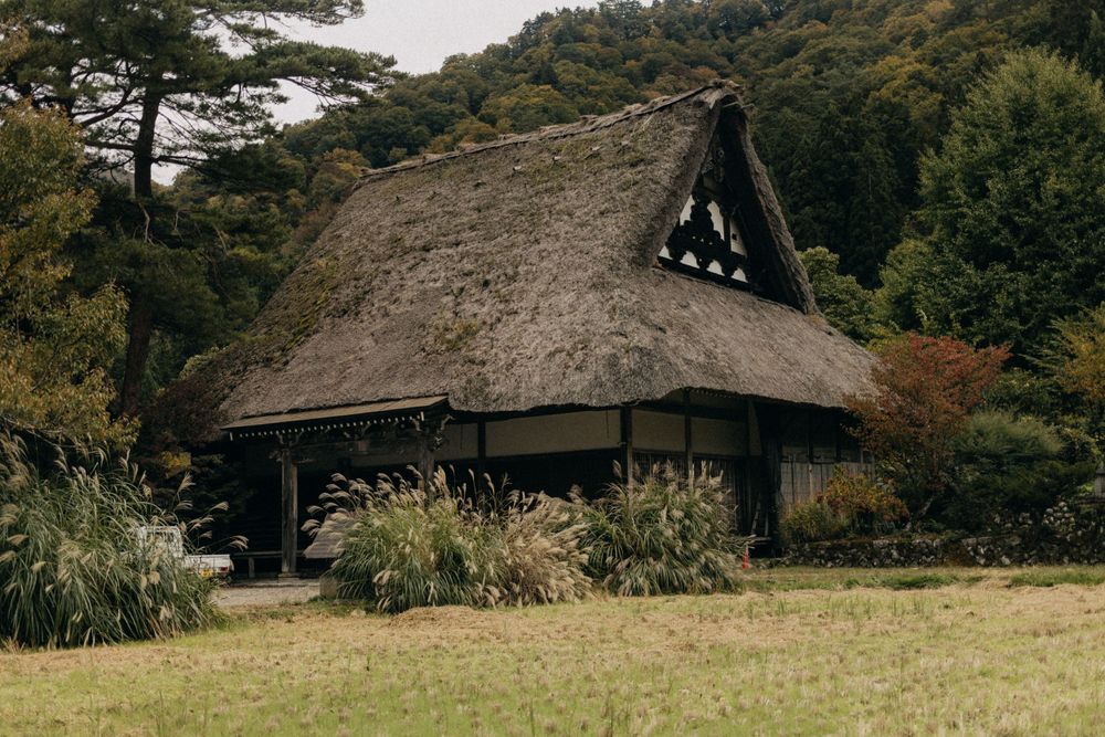 Large thatched-roof gassho-zukuri house with traditional Japanese architecture in a rural setting.