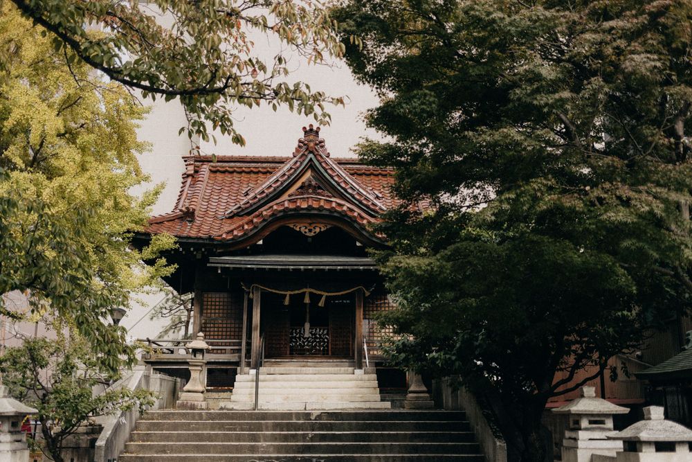 Traditional Japanese temple with wooden architecture surrounded by lush trees and stone lanterns.
