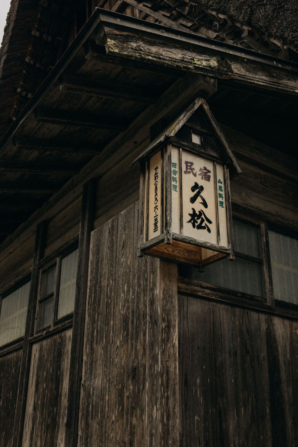 Vintage wooden Japanese lantern with kanji characters mounted on weathered traditional building exterior.