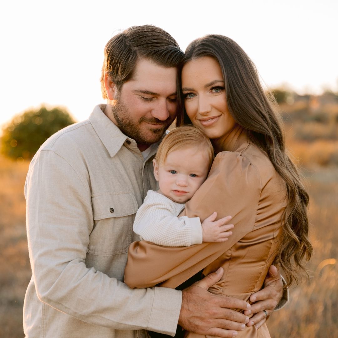 Family embraces together in golden sunlight during outdoor portrait session at sunset.