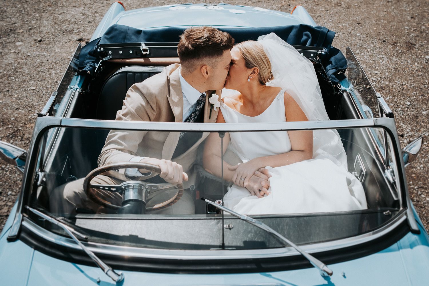 Newlyweds share a romantic moment in a classic blue convertible car on their wedding day.