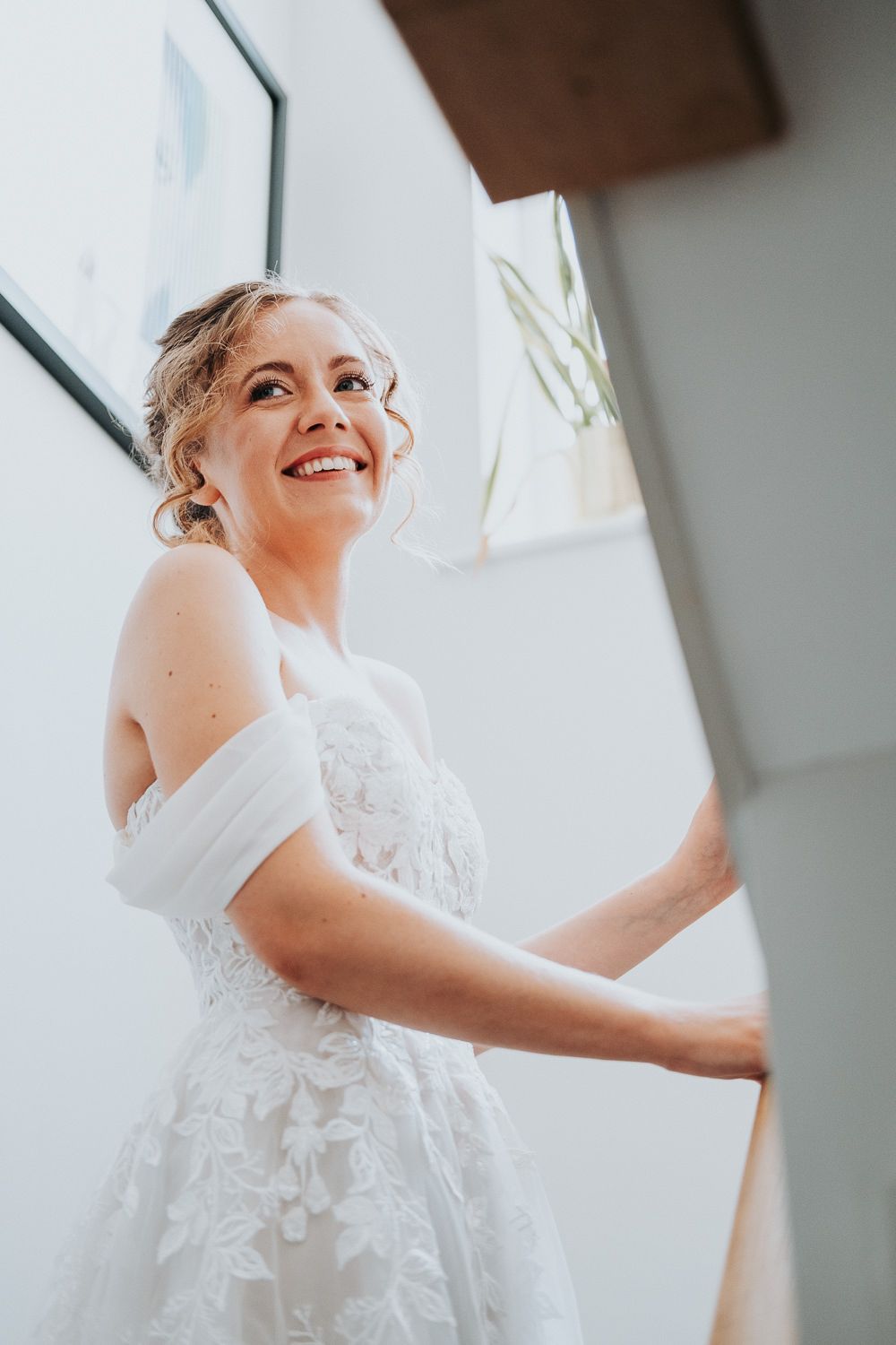 Bride in off-shoulder lace wedding dress smiles while getting ready.