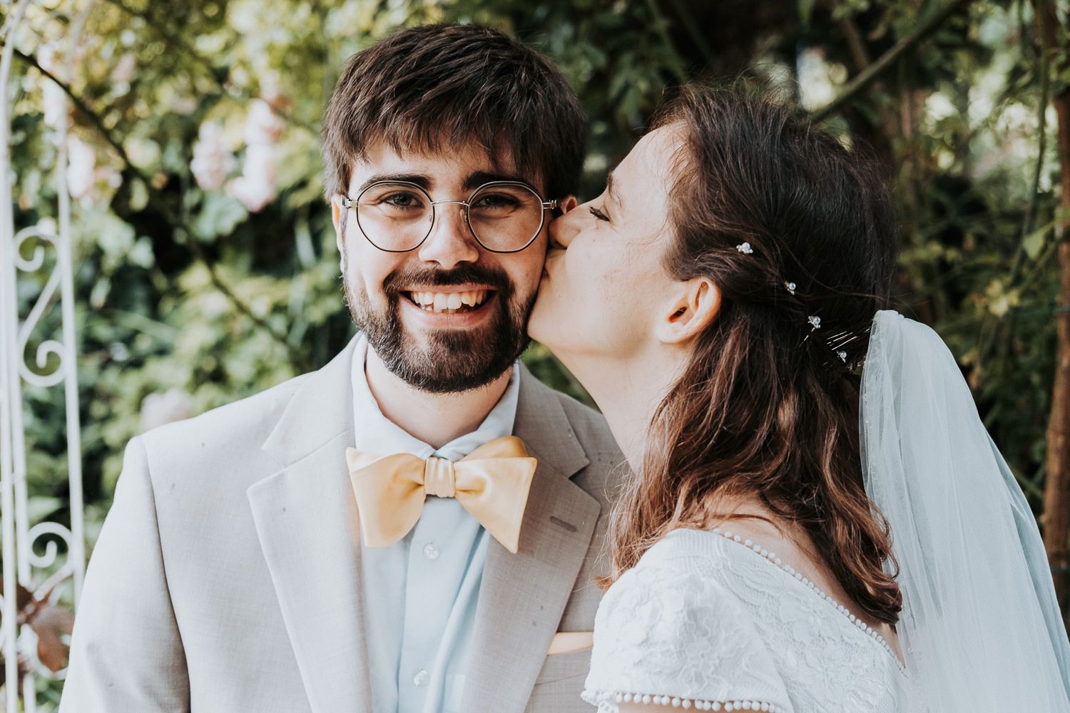 Wedding couple shares tender moment in garden setting with groom in light suit and bow tie.