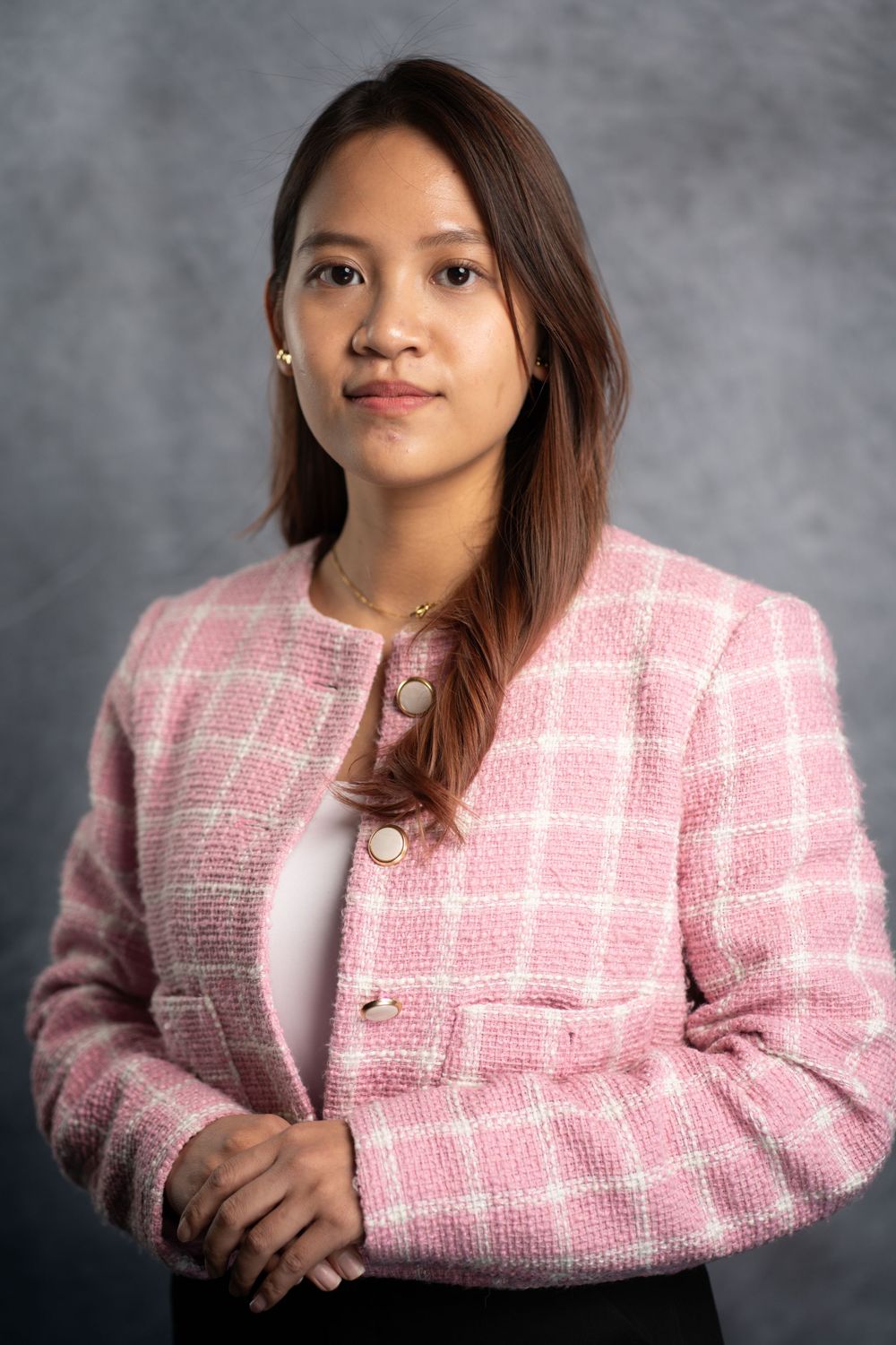 Professional portrait of someone posing in a pink tweed blazer and white top against a grey background.