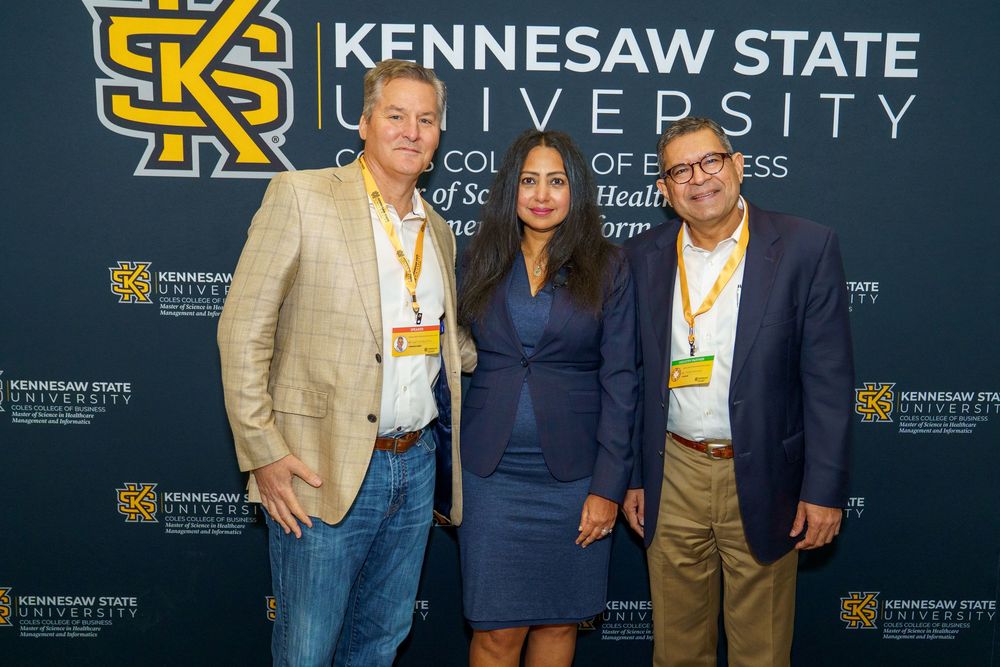 Three people pose together at a Kennesaw State University branded backdrop during an event.