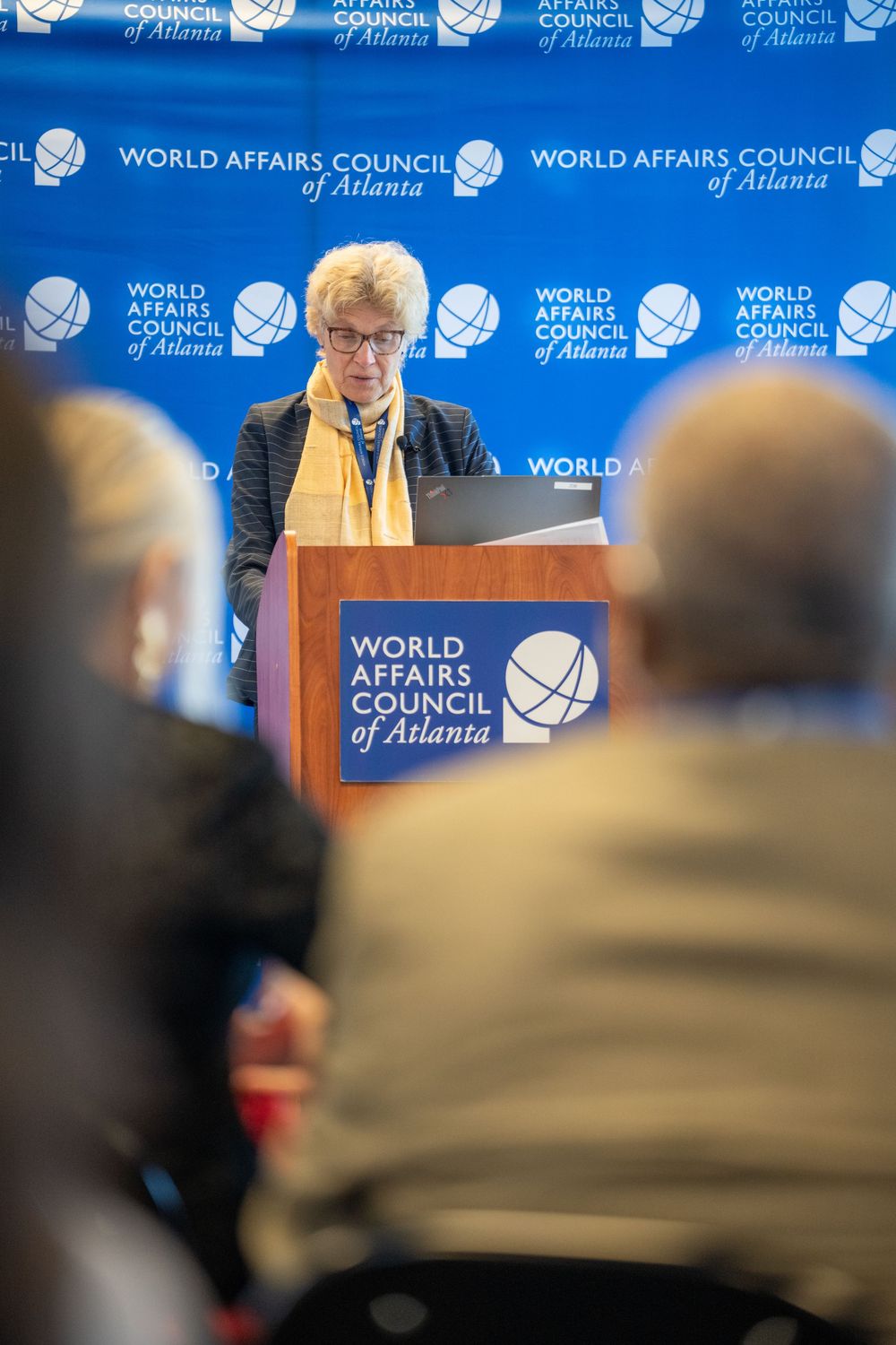 A speaker stands at a podium during a World Affairs Council of Atlanta event with organization logos visible in background.