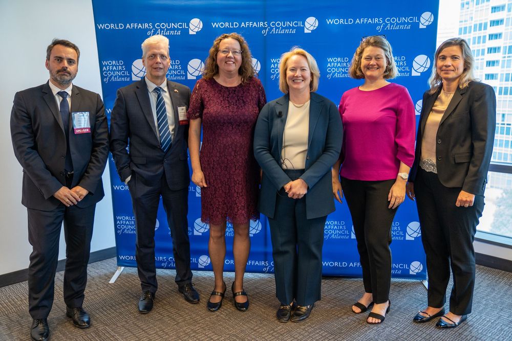 Six professionals pose together at a World Affairs Council event in front of a branded backdrop.