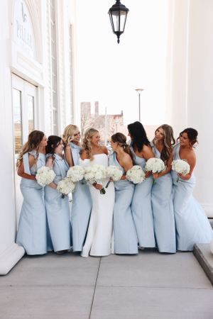 Bridal party in light blue dresses poses together holding white bouquets.