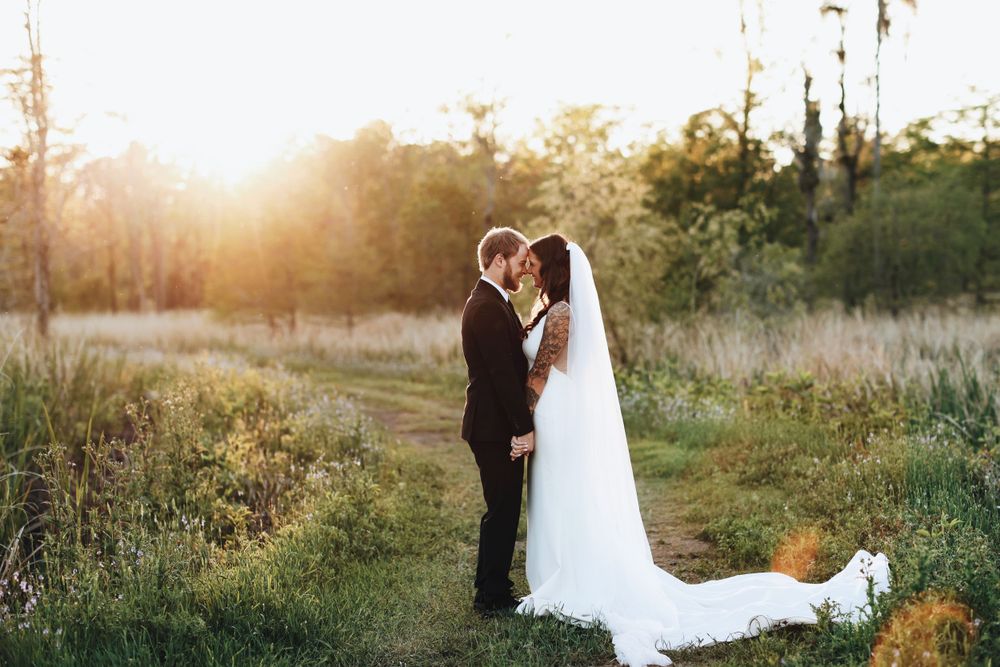 Newlyweds share intimate moment at sunset in field with beautiful glowing light.