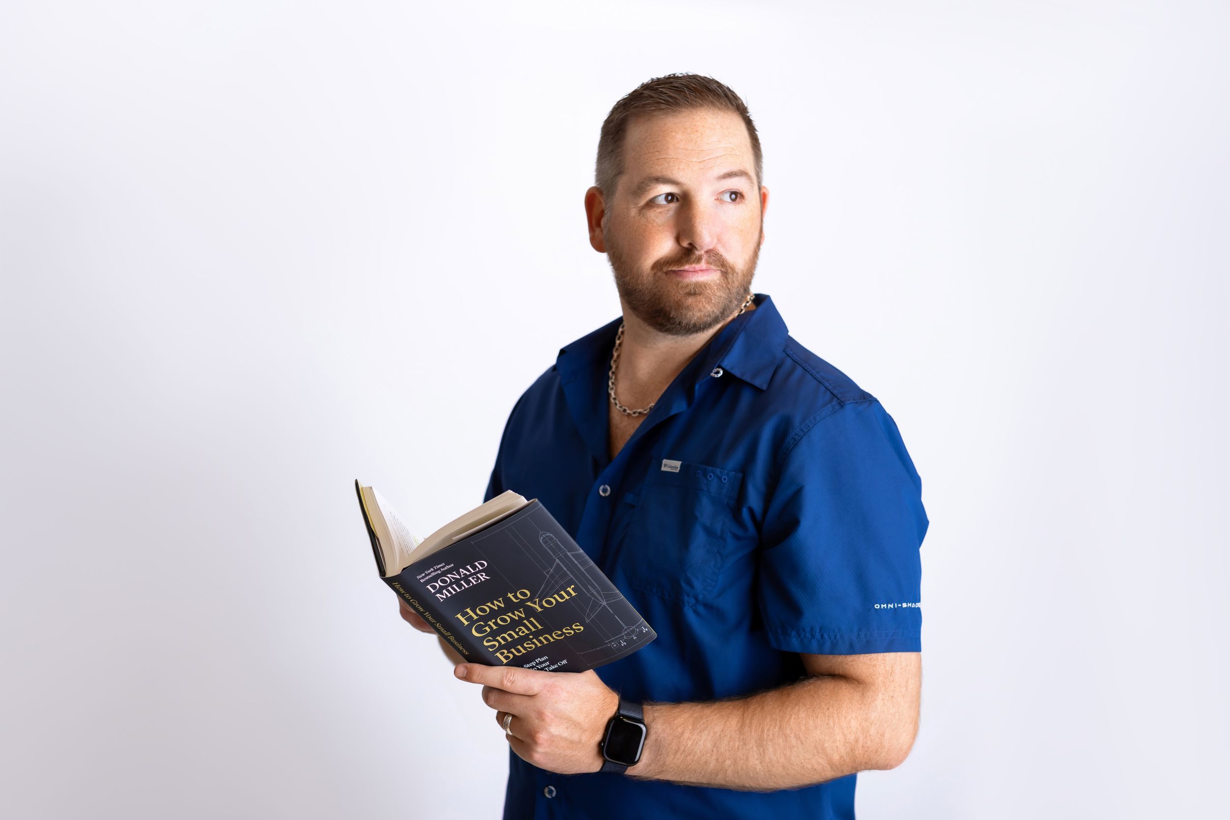 A person wearing a blue polo shirt holds an open book against a white background.