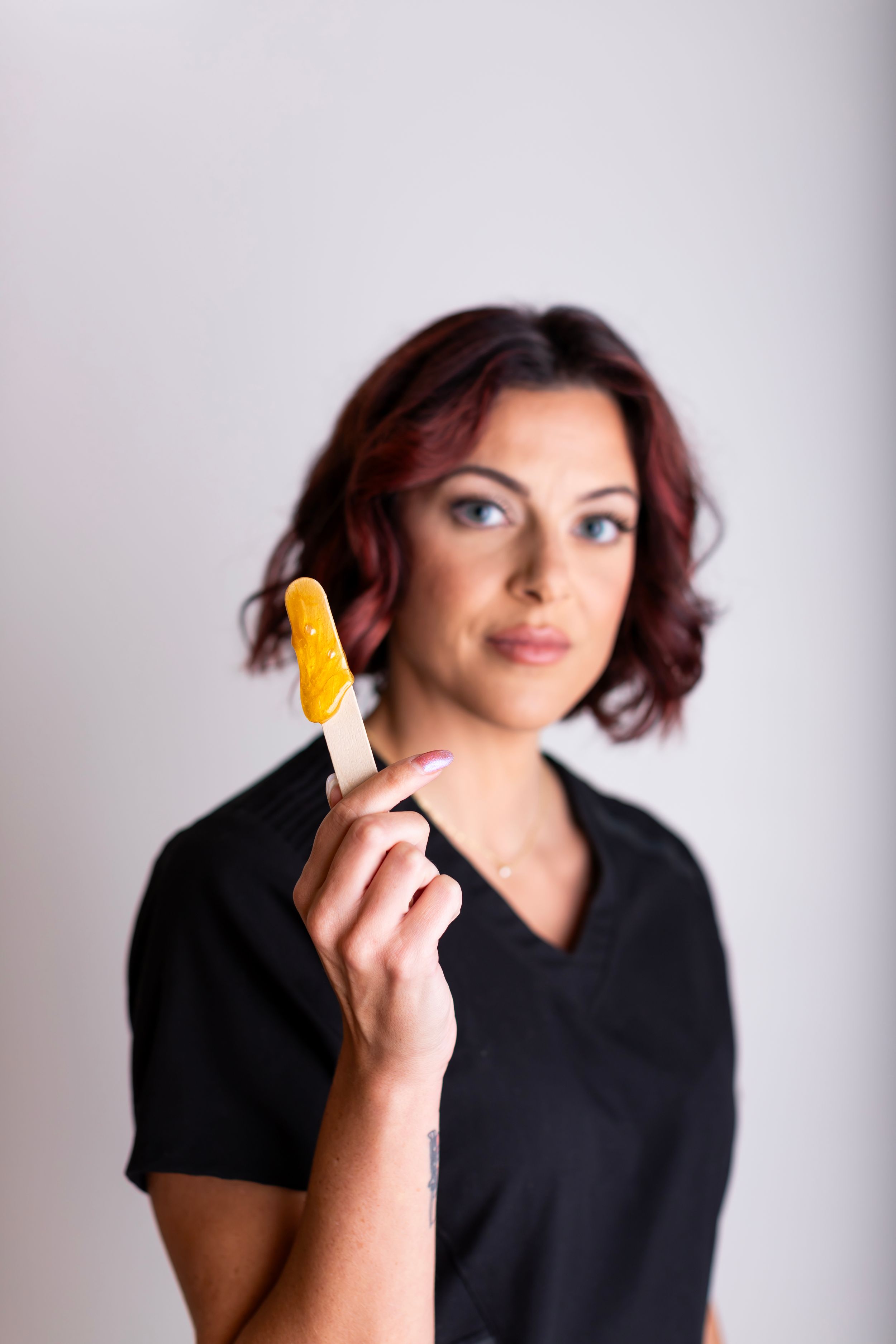 A person in a black shirt holds up a yellow popsicle or ice cream bar against a light gray background.