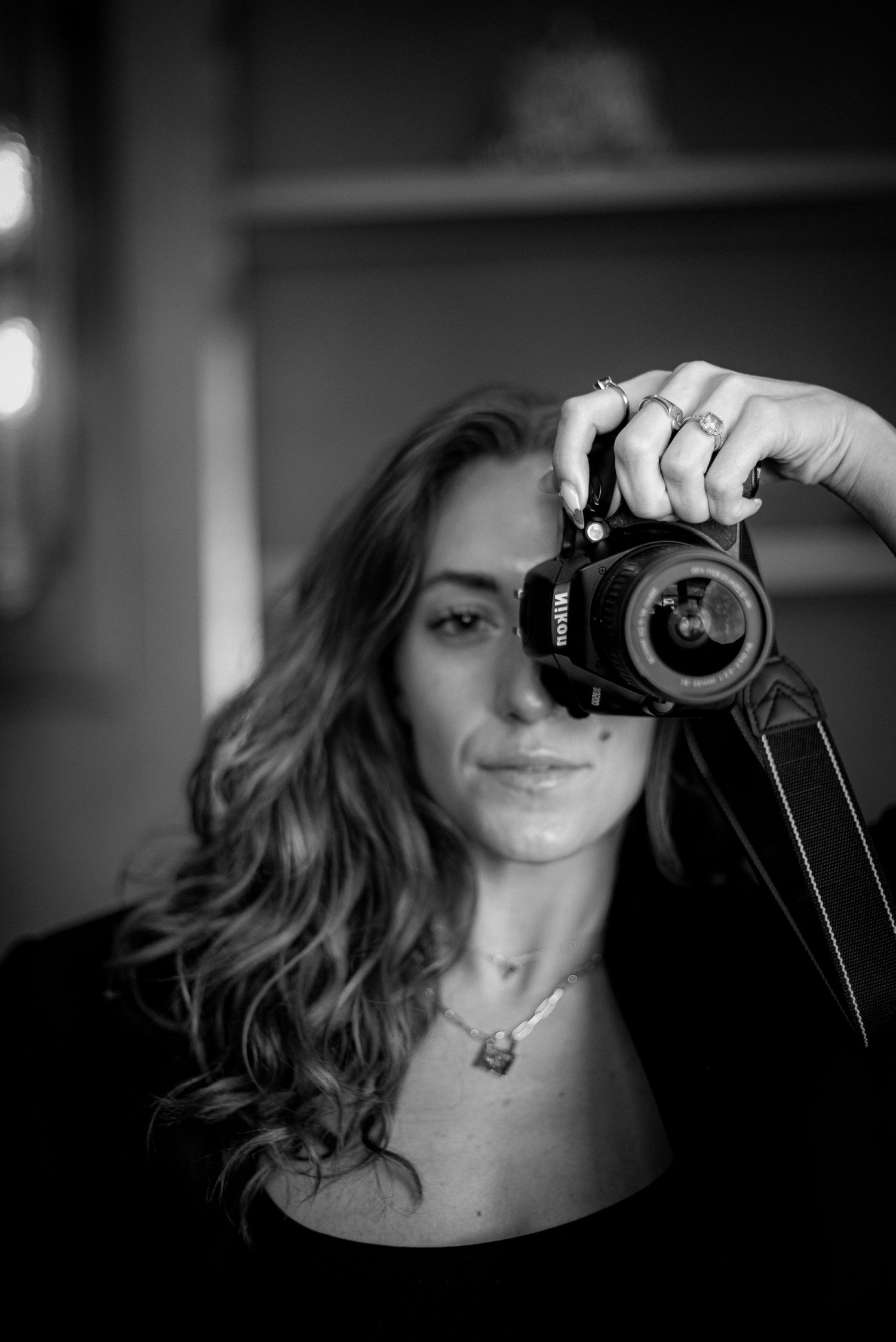 Black and white photo of someone taking a self-portrait with a DSLR camera in moody lighting.