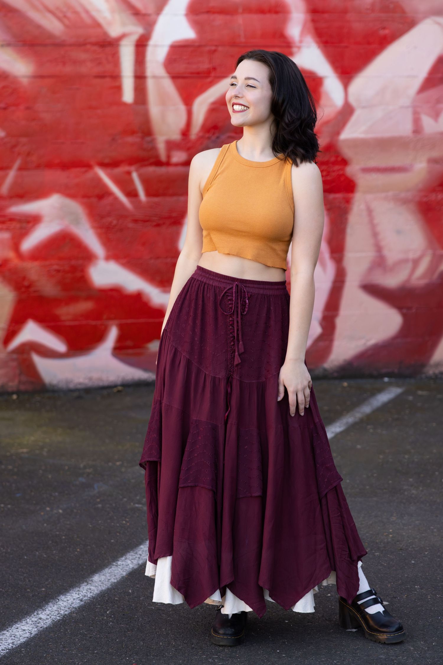 Fashion portrait of person in mustard crop top and burgundy maxi skirt posing against red graffiti wall.