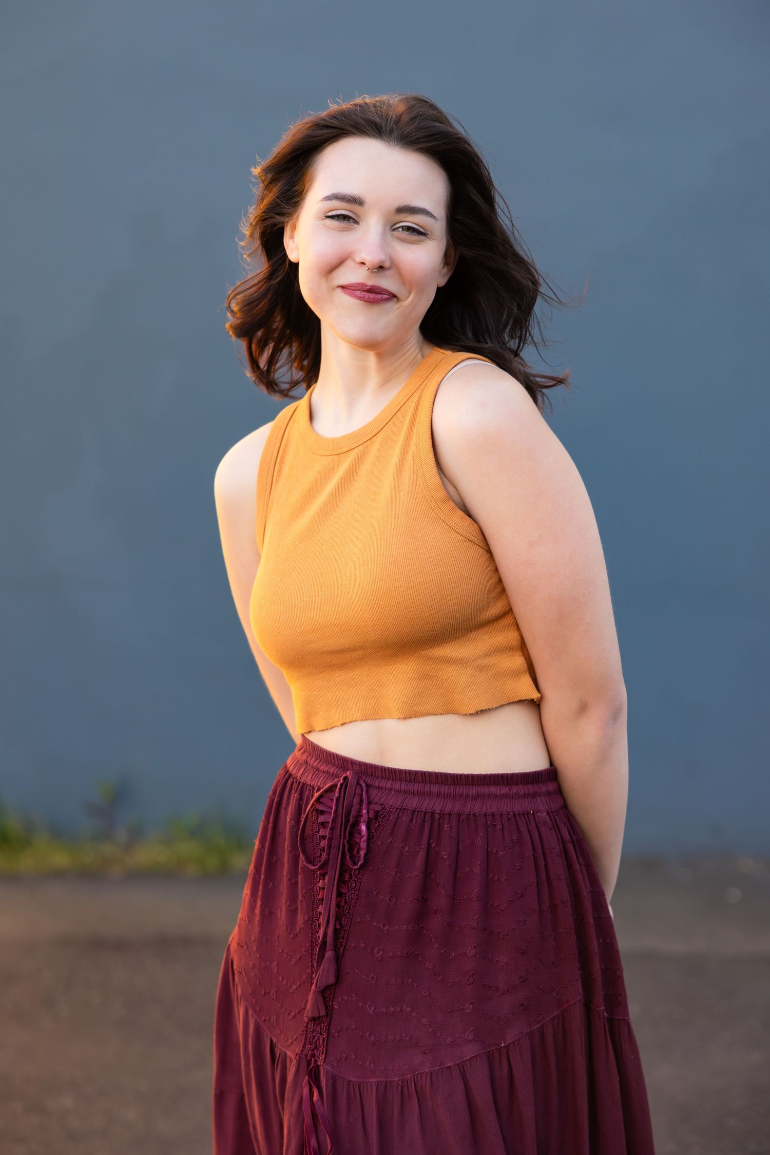 Someone wearing an orange crop top and burgundy maxi skirt smiles outdoors against a dark background.