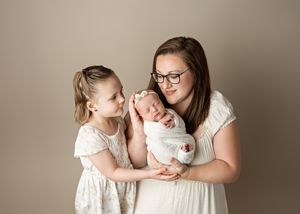 A heartwarming portrait of a parent with two children wearing white, captured against a neutral studio backdrop.