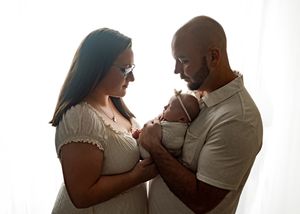 A loving couple holds their newborn baby together in a tender backlit moment at home.