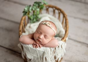 Sleeping newborn rests peacefully in vintage wooden barrel chair with white fabric and delicate headband.