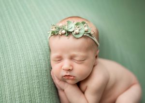 Sleeping newborn wearing a delicate mint floral headband rests peacefully on a sage green textured blanket.