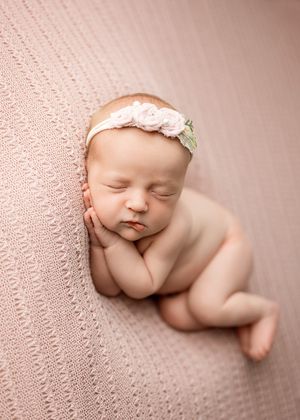 Peaceful newborn resting on textured pink fabric with rose headband in artistic portrait style.