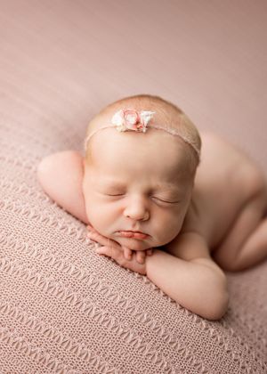 Peaceful sleeping newborn wearing delicate pink headband rests on soft textured pink knit blanket.