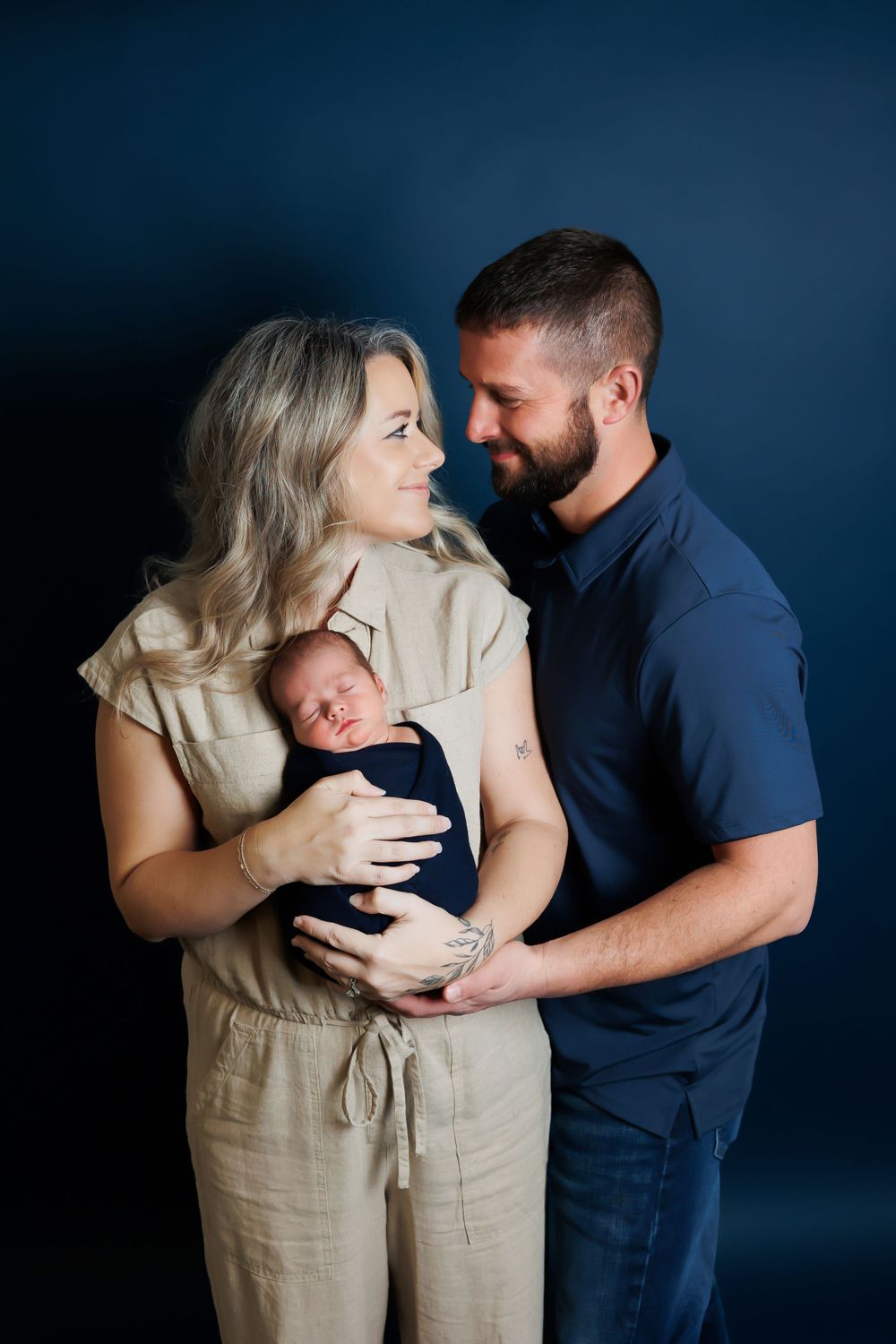 A family shares an intimate moment together against a dark blue backdrop as they hold their newborn baby.