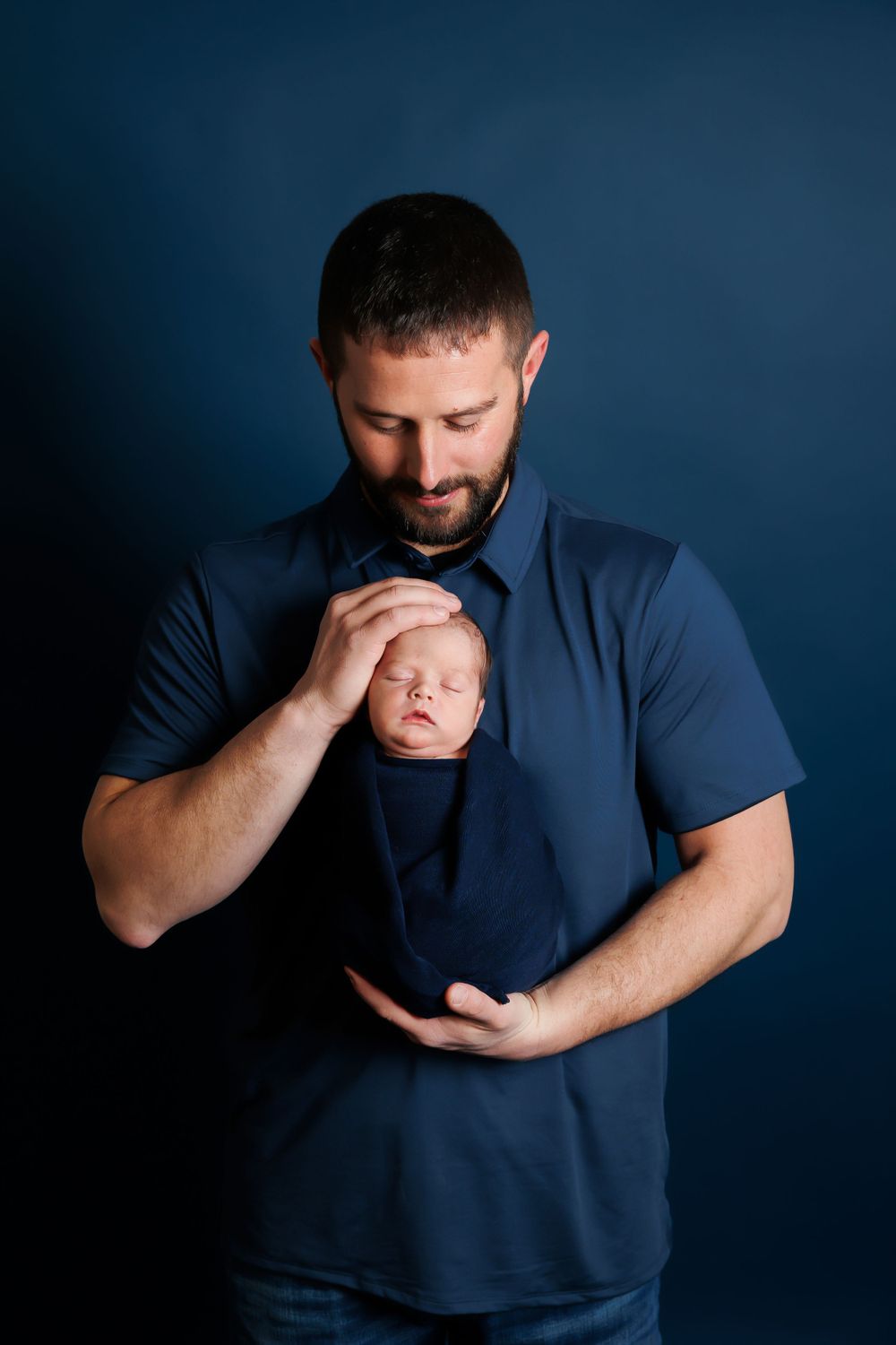 A tender moment between a parent and newborn baby wearing matching navy blue outfits.