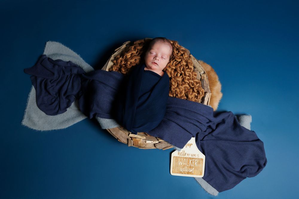 Sleeping newborn baby wrapped in navy fabric lying on a blue background with curled edges.