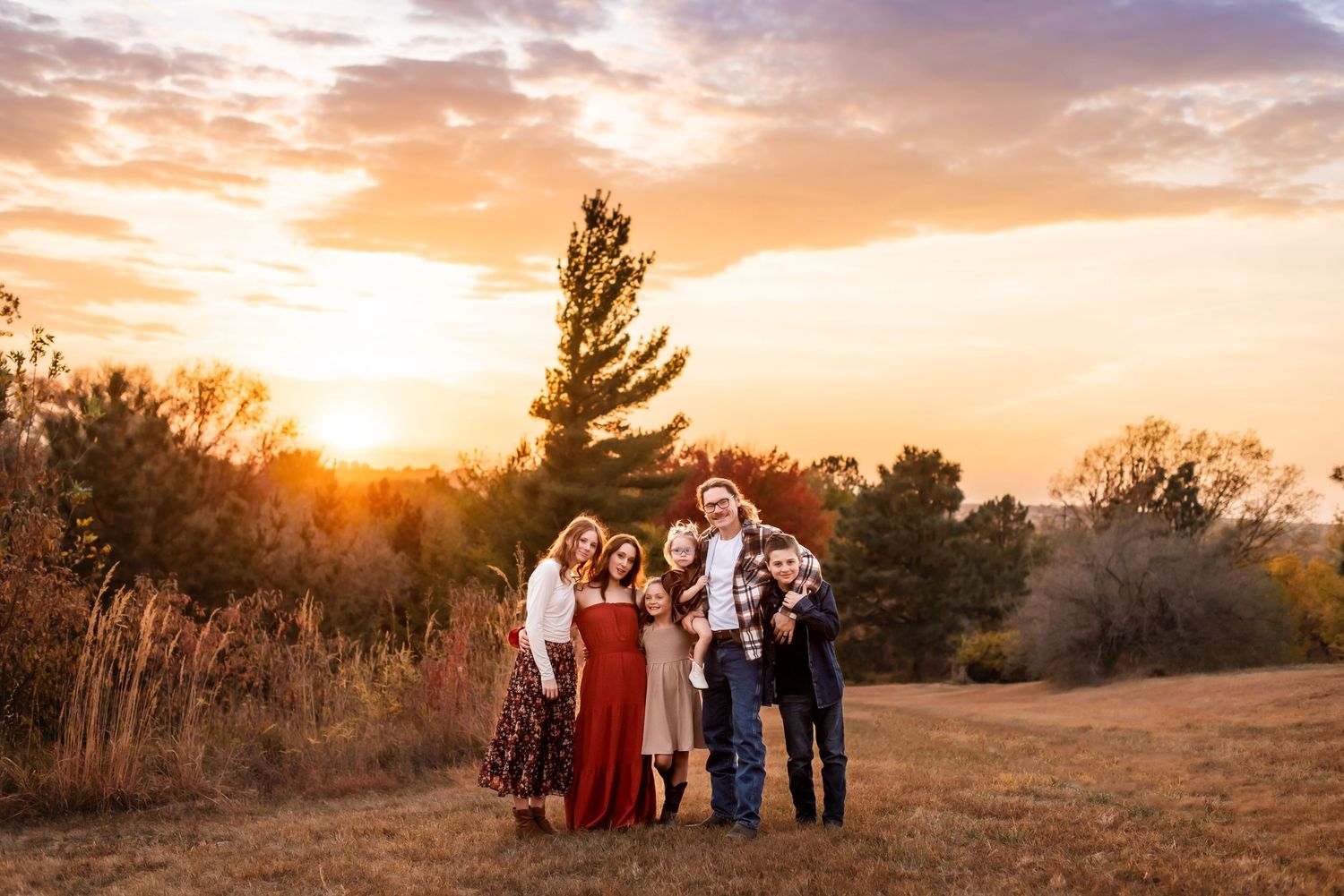 A group stands together on a hilltop against a dramatic golden sunset with trees silhouetted in the background.