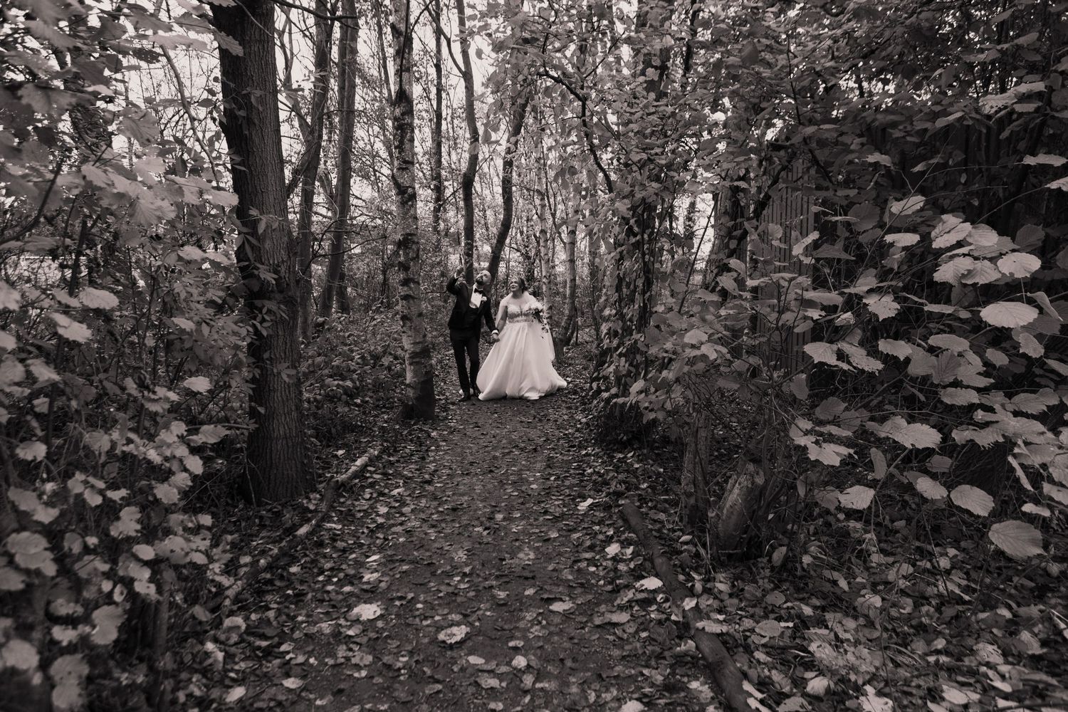 A dreamy black and white photo shows a path through the woods with a wedding dress figure in the distance.