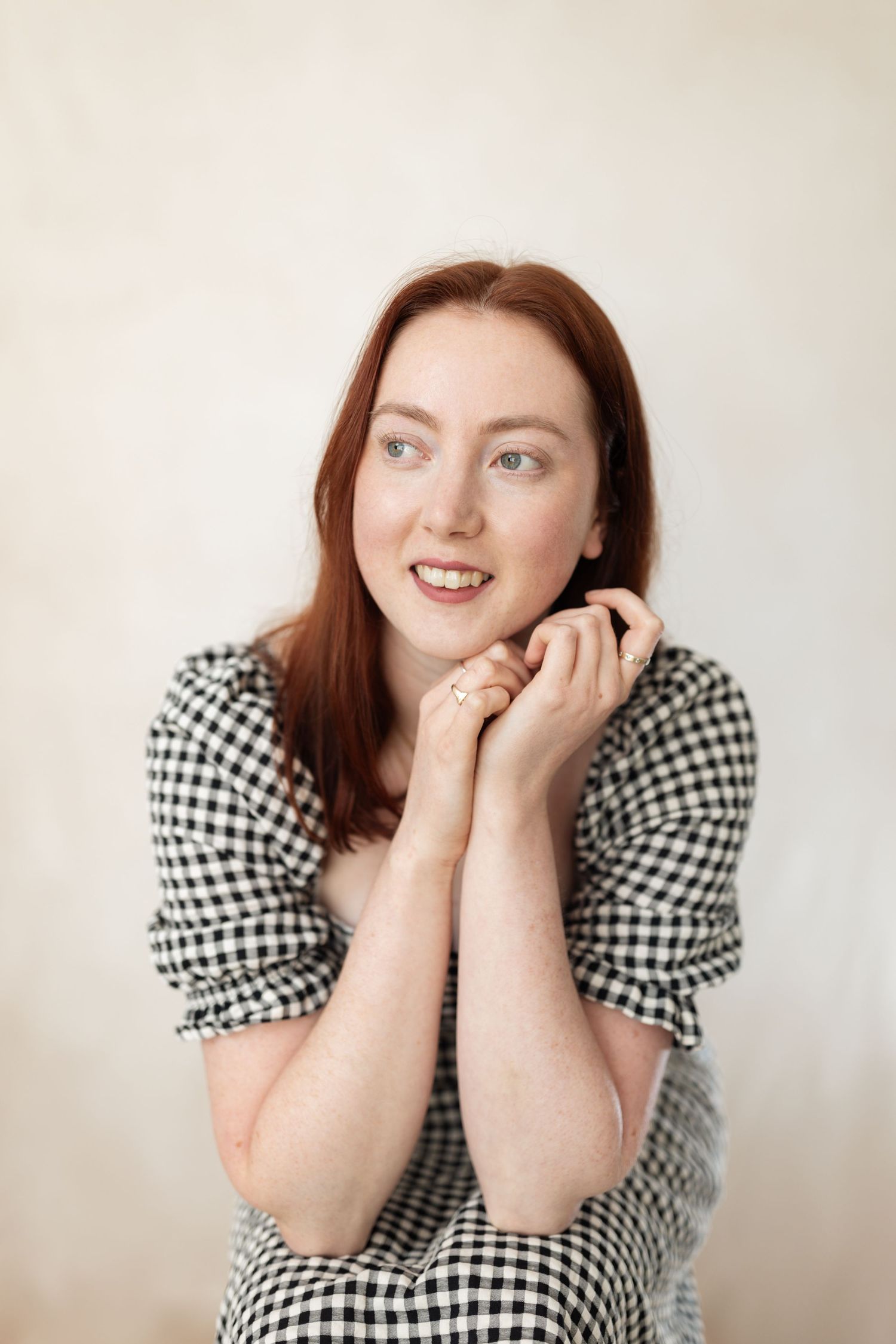 A woman in a floral dress sits on a wooden chair against a light backdrop.