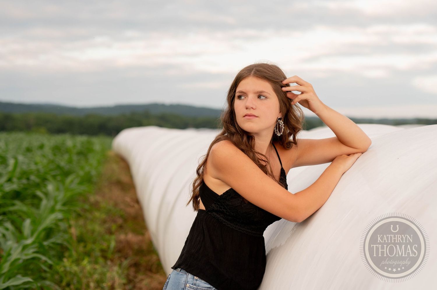 Person in a black top poses against a white bale in a green field at sunset.
