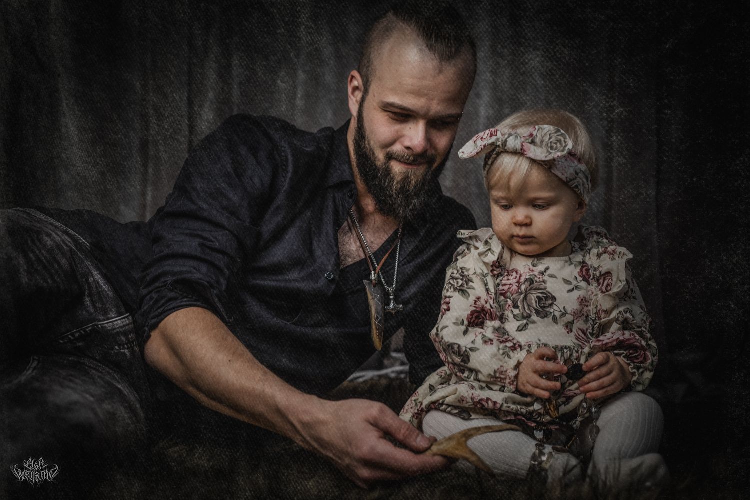 A moody portrait of an adult and small child reading together against a dark background.