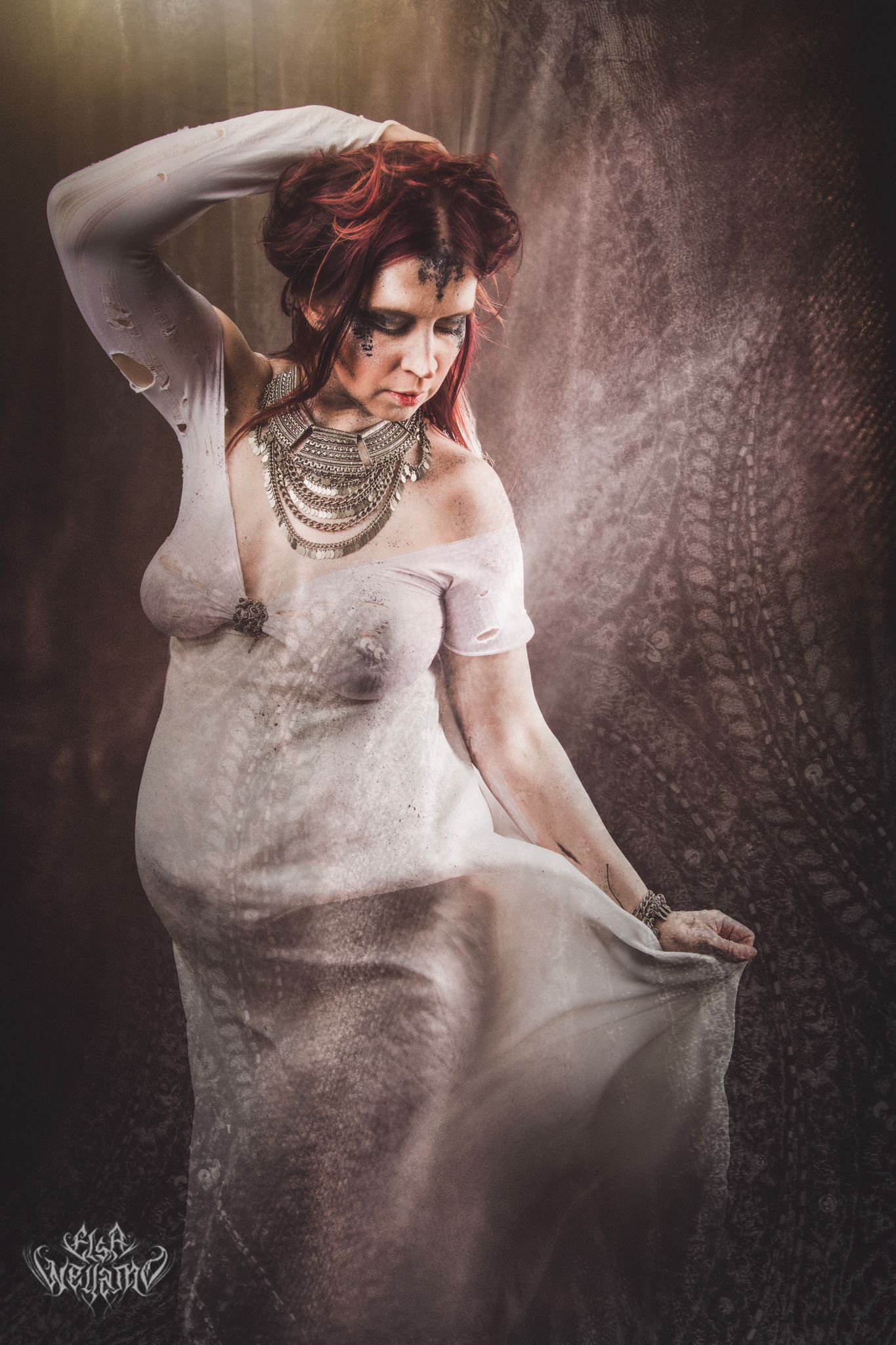 A figure in a white dress poses against a dark background with dramatic lighting and layered necklaces.