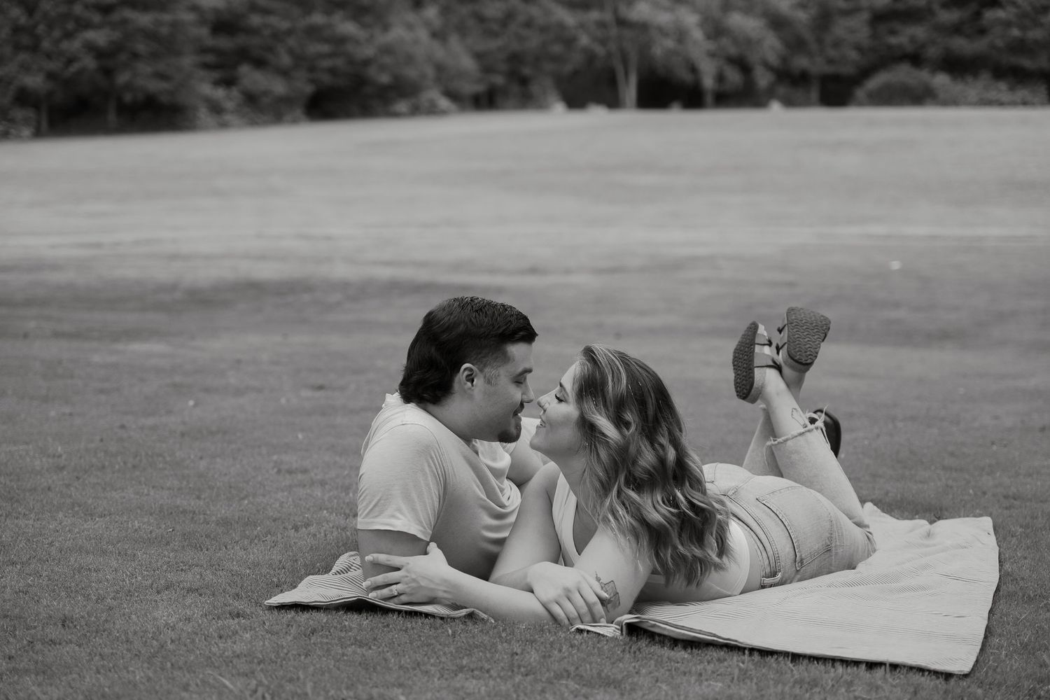 A couple lounges together on a blanket in a grassy field in black and white.