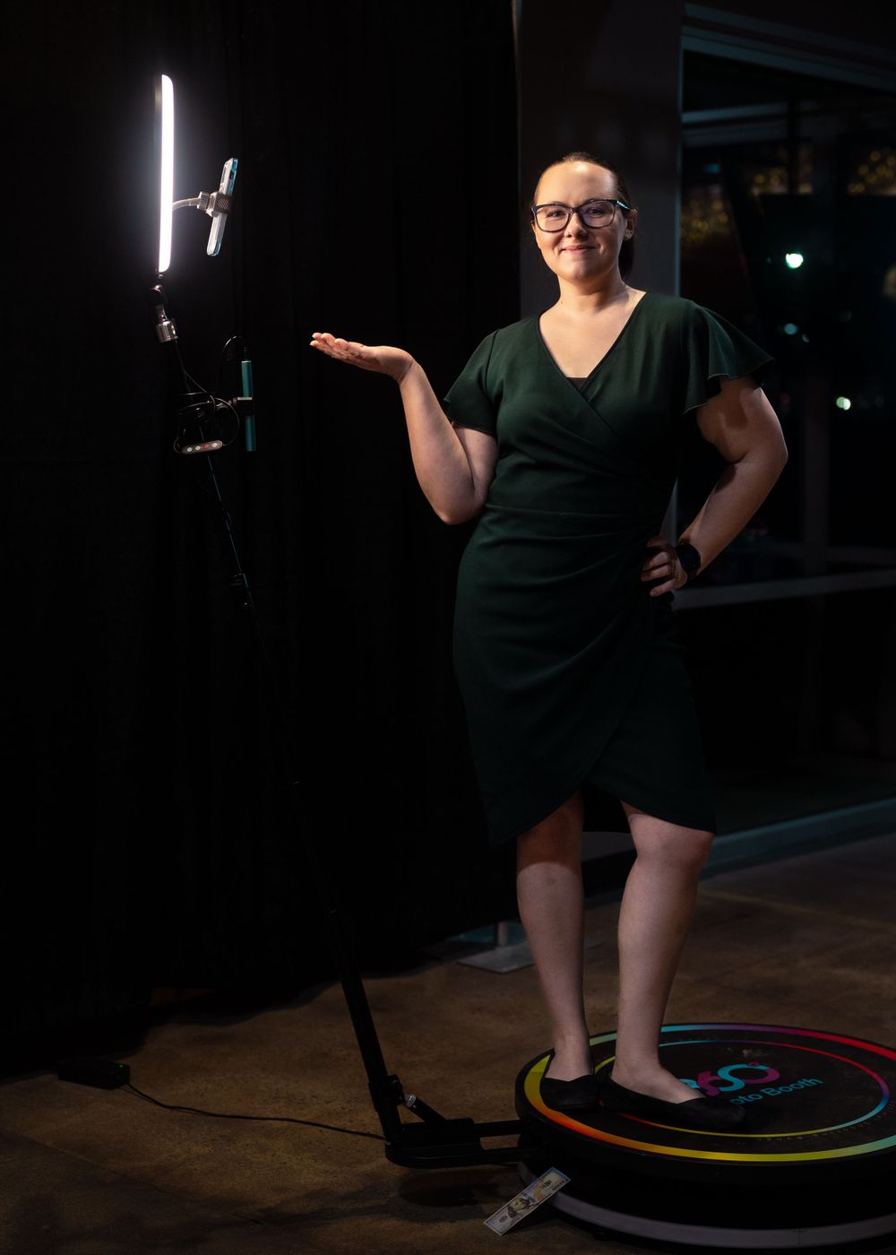 A person in a green dress stands in front of a ring light and camera setup with a circular RGB light on the floor.