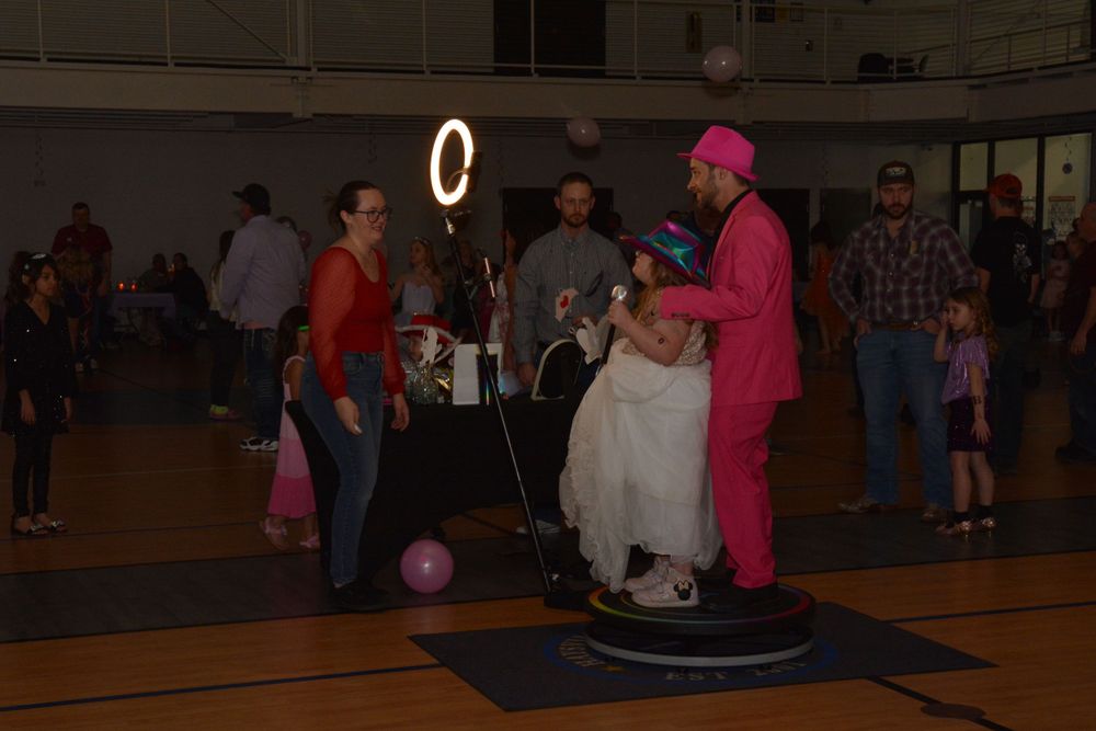 People dancing at a community event in a gymnasium with colorful lighting and festive decorations.