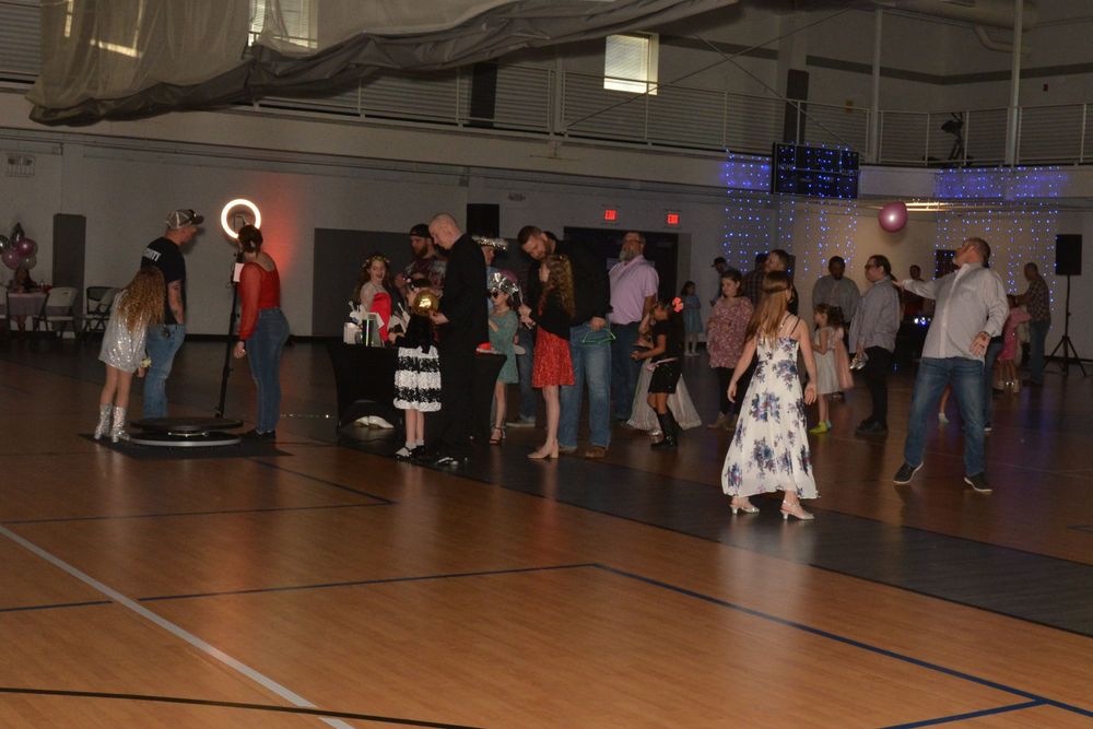 A group gathered in a dimly lit gymnasium for a social dance event with colored spotlights.