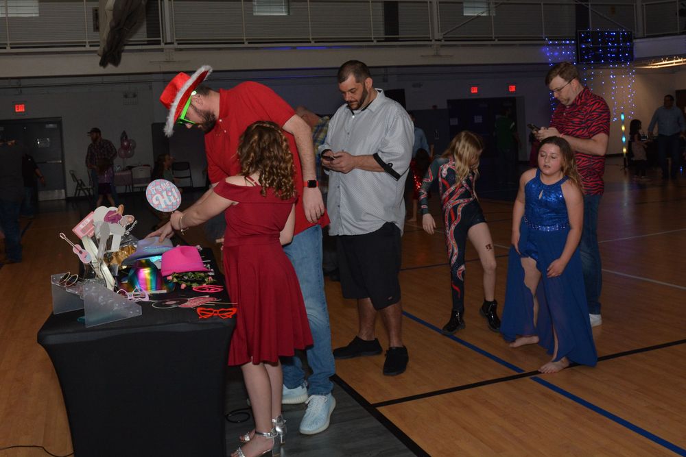 People line up at a table during an event in a school gymnasium with low lighting.