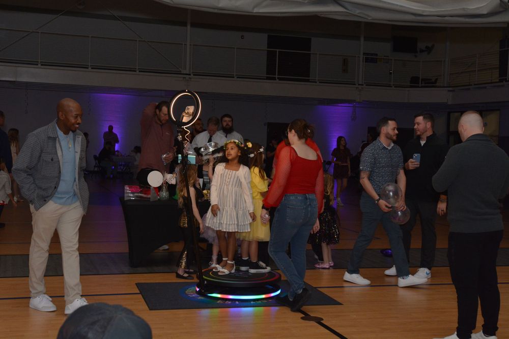 People gather on a dance floor with purple lighting and LED hoop entertainment at an indoor party venue.