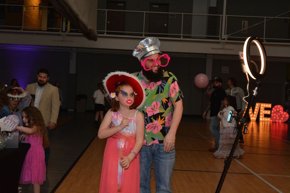 People dance at an indoor party with glowing decorations and LED ring lights in a dimly lit space.