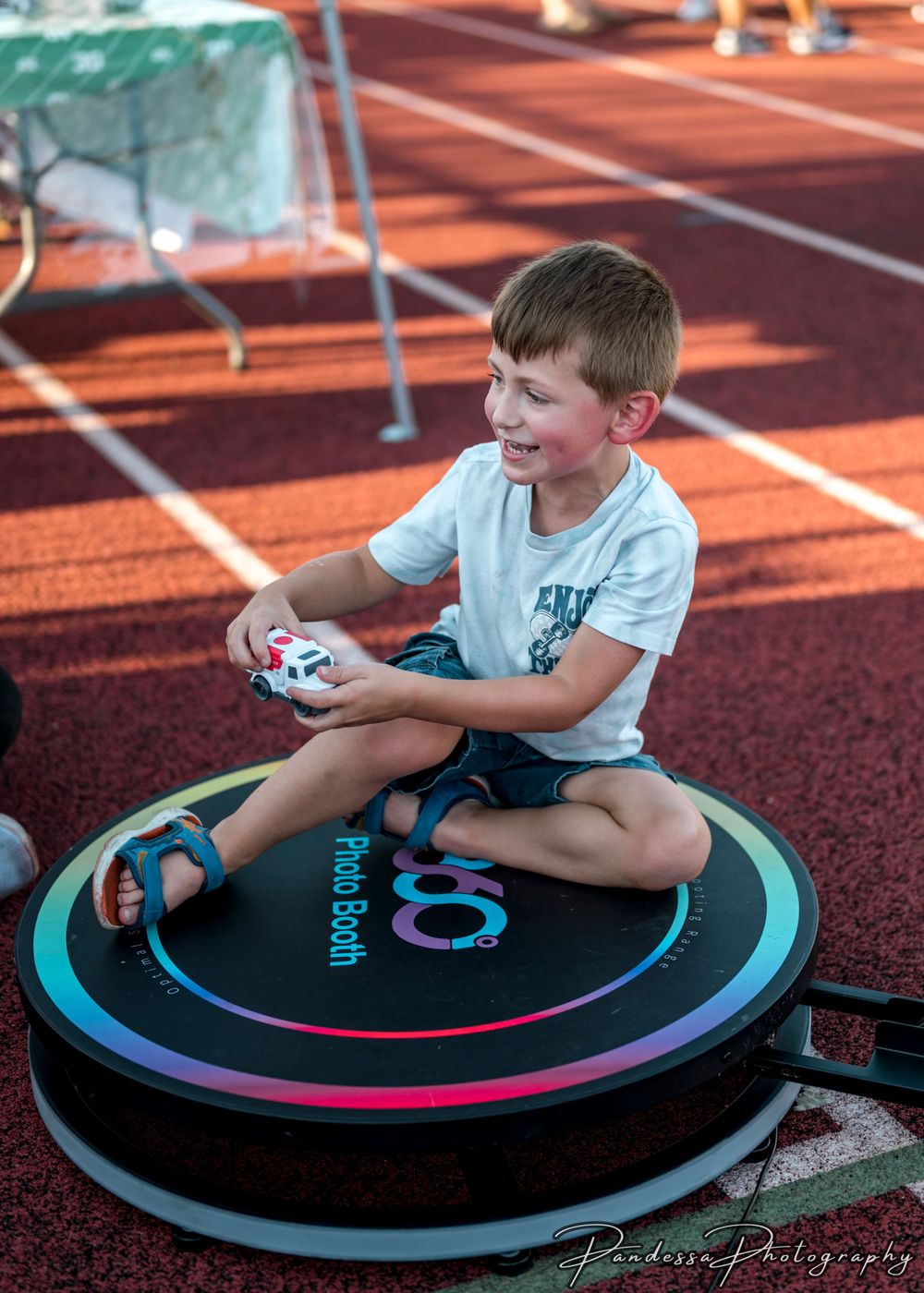 Happy young child sitting cross-legged on a vibrant fitness trampoline at an indoor sports facility with running tracks.