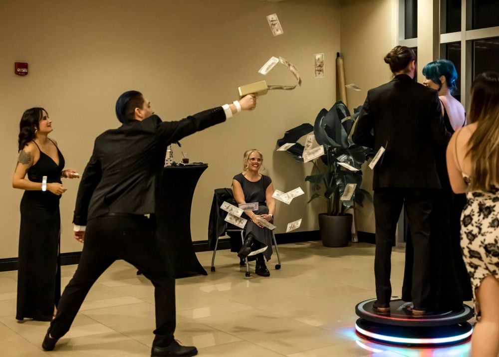 People participate in a theatrical scene at a formal event with papers flying through the air in a lobby space.