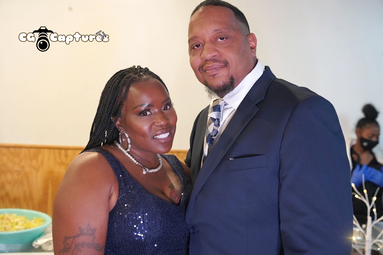A couple poses together at an event, with one wearing a sparkly purple dress and the other in a dark suit and tie.